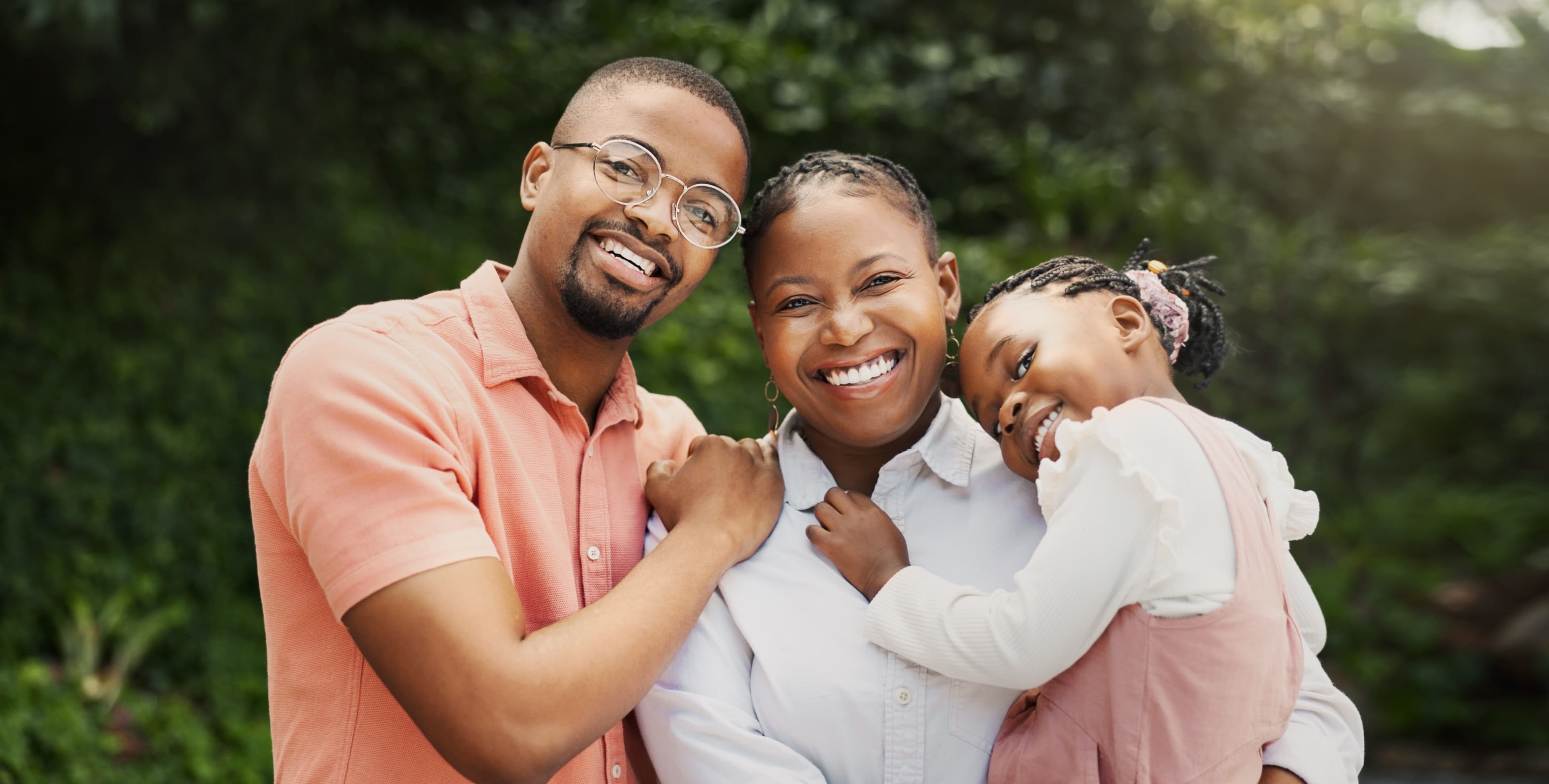 A father, mother, and daughter smiling together outdoors